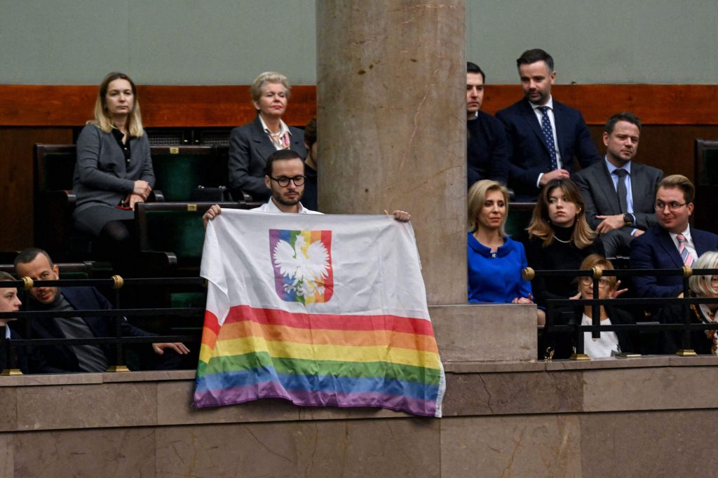 Bart Staszewski brandit un drapeau aux couleurs LGBT+ à l'Assemblée lors du discours de politique générale de Donald Tusk.