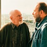 Les deux acteurs du film Les Tortues Olivier Gourmet et Dave Johns face à face devant une baie vitrée