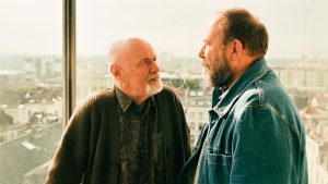 Les deux acteurs du film Les Tortues Olivier Gourmet et Dave Johns face à face devant une baie vitrée