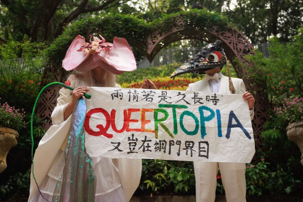 L'artiste performeur non-binaire Holok Chen (à gauche) et un mannequin brandissent une banderole promouvant l'égalité LGBTQ devant un registre des mariages à Hong Kong.